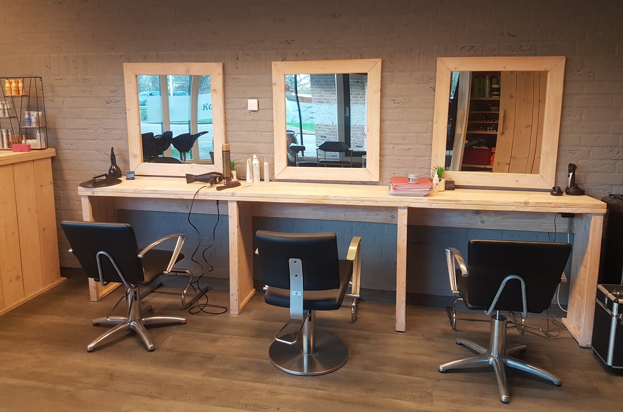 De salon van Sandra’s Hairfashion: drie spiegels in houten lijsten boven een houten werkblad, met drie zwarte kappersstoelen